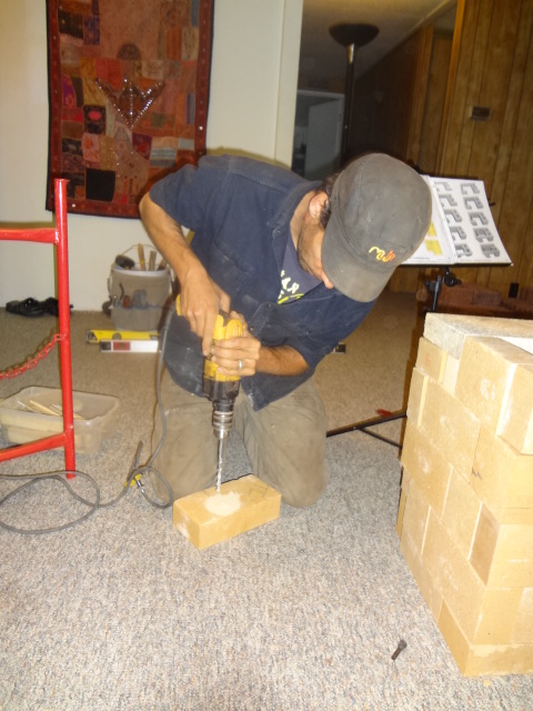 Max drills a hole in the brick to sink the bolt, into which the screw will be threaded